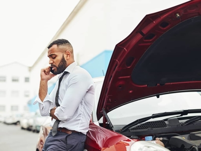 a man on the phone leaning on a broken down car