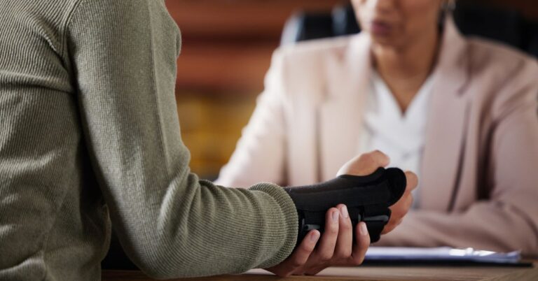 Man with brace on wrist sits across from woman.