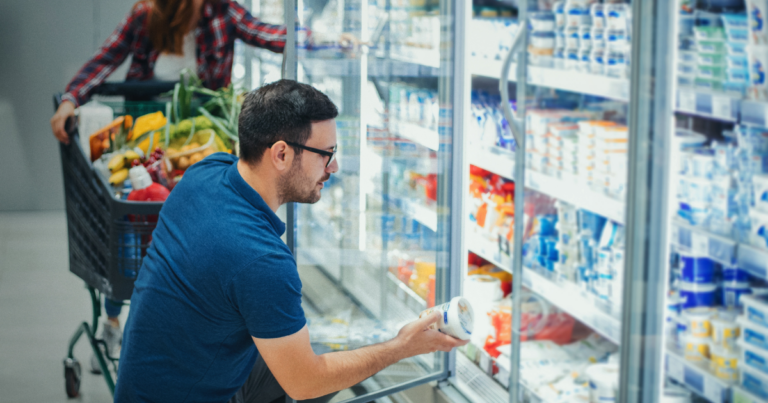 Man at grocery store looks through refrigerated section.